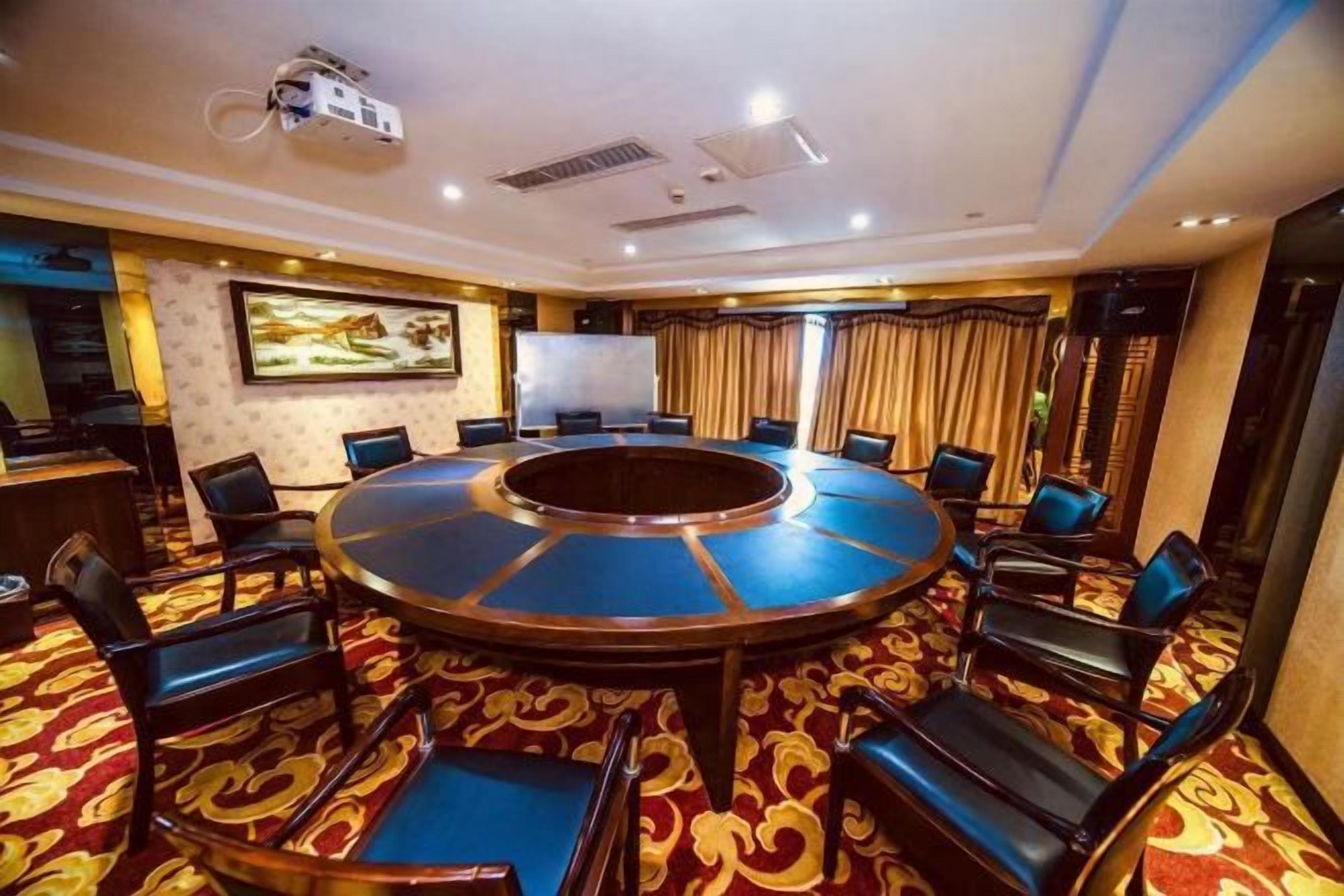 A conference room with a round table, chairs, a projector, and a large screen.