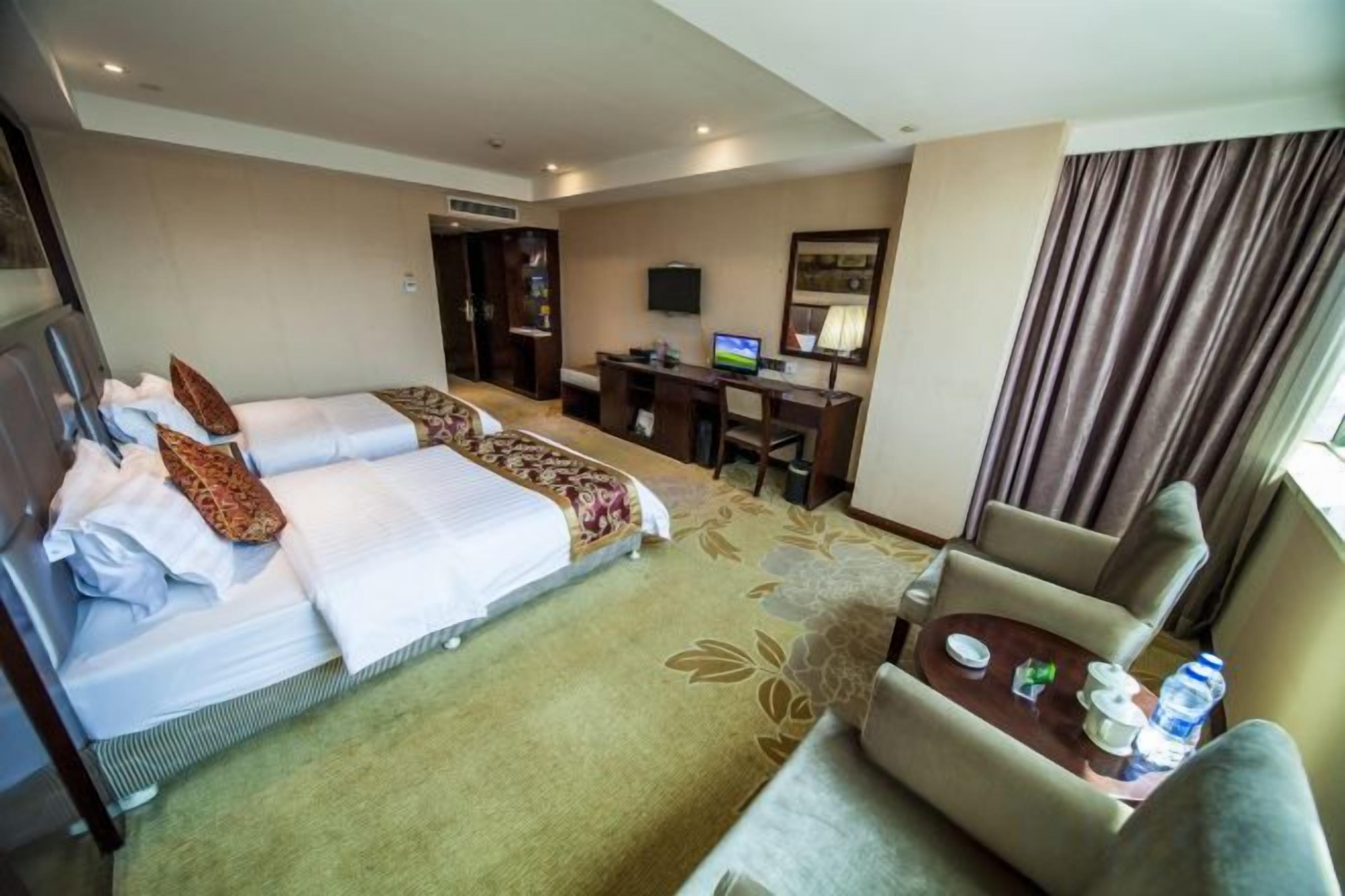 A hotel room with a bed, desk, chair, and a small table with a bottle.