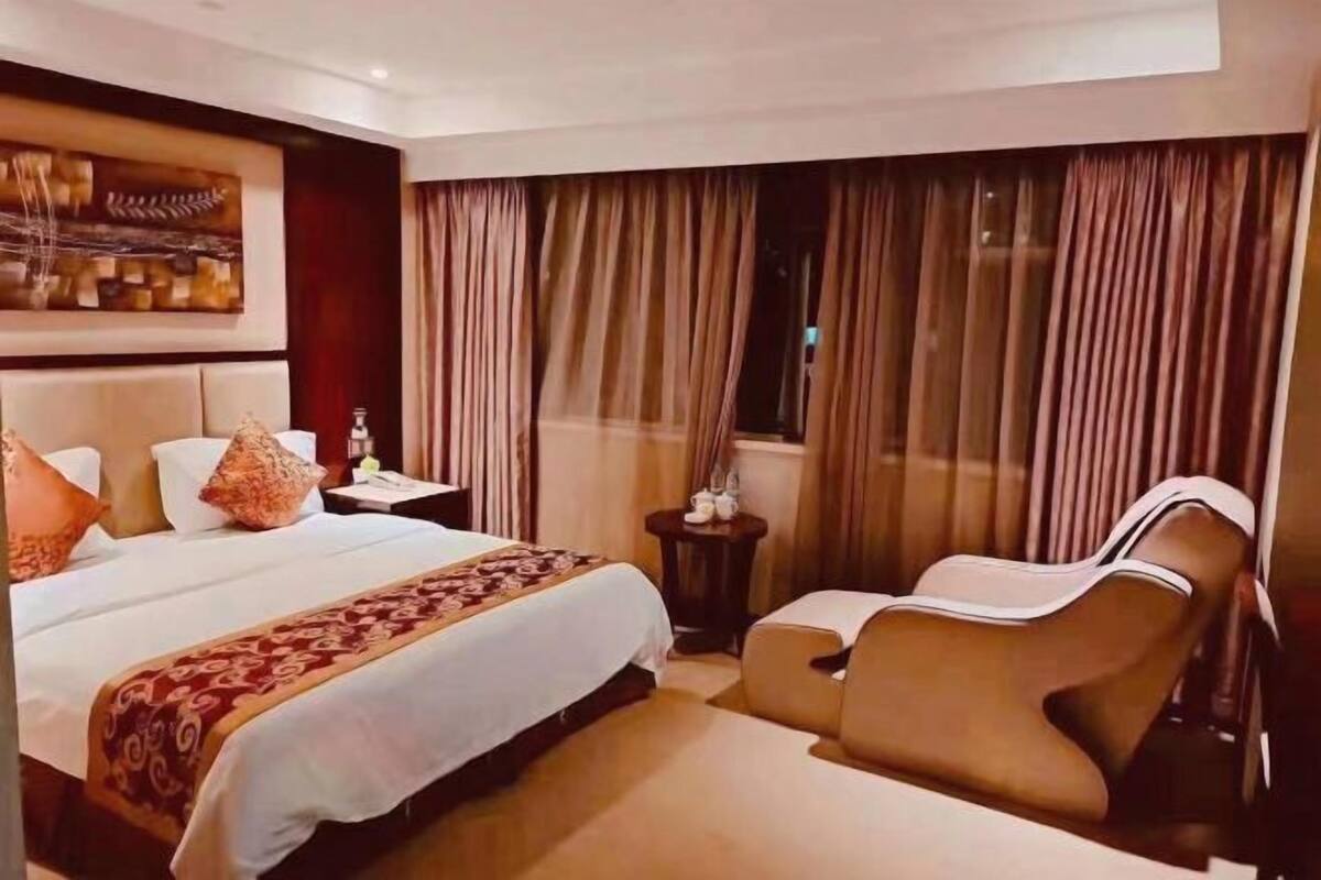 A hotel room with a large bed, a sofa, a nightstand, and a painting on the wall.
