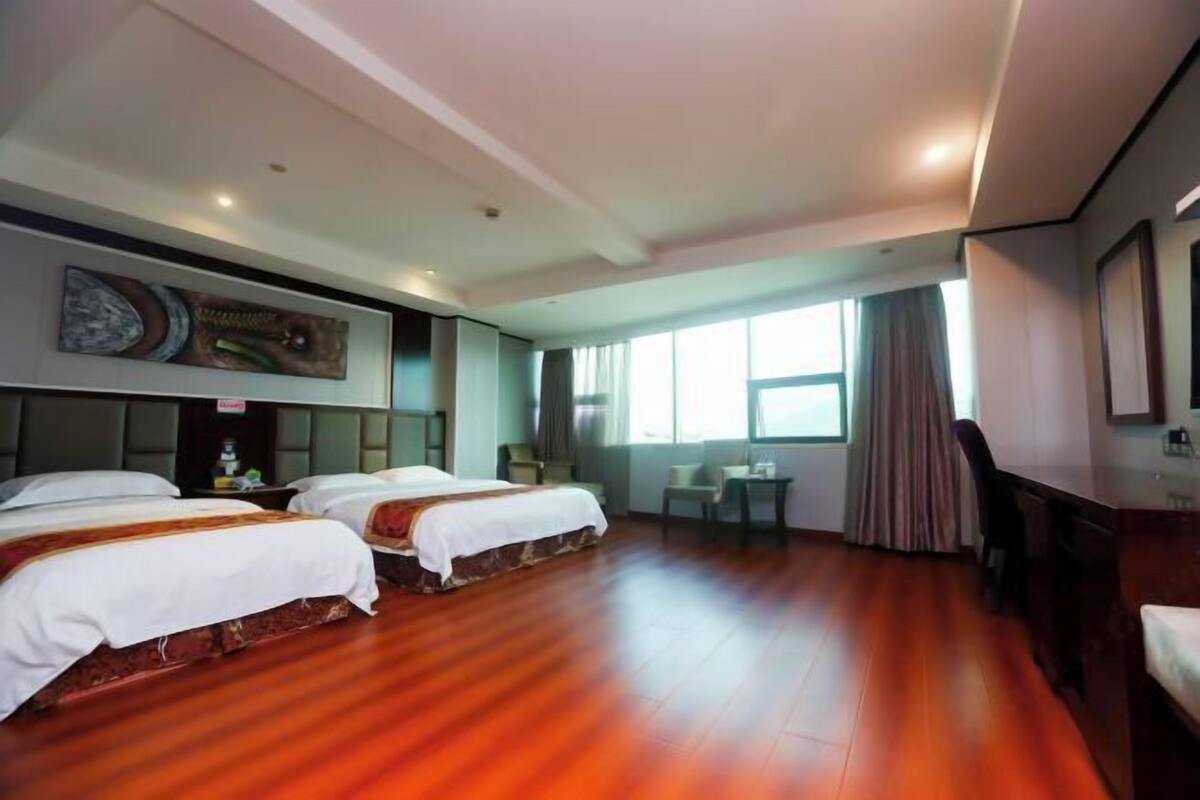 A hotel room with two beds, a desk, a chair, a small table, and a window with curtains.