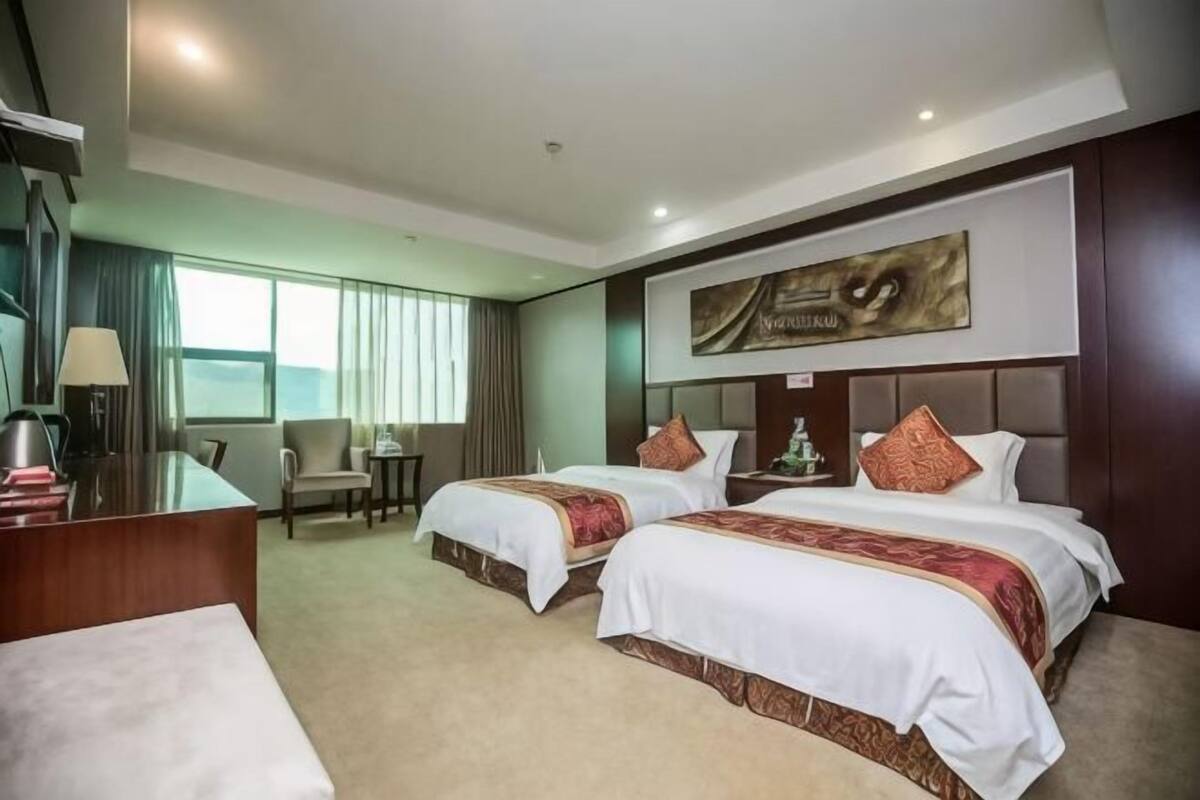 A hotel room with two beds, a desk, a chair, and a large window.