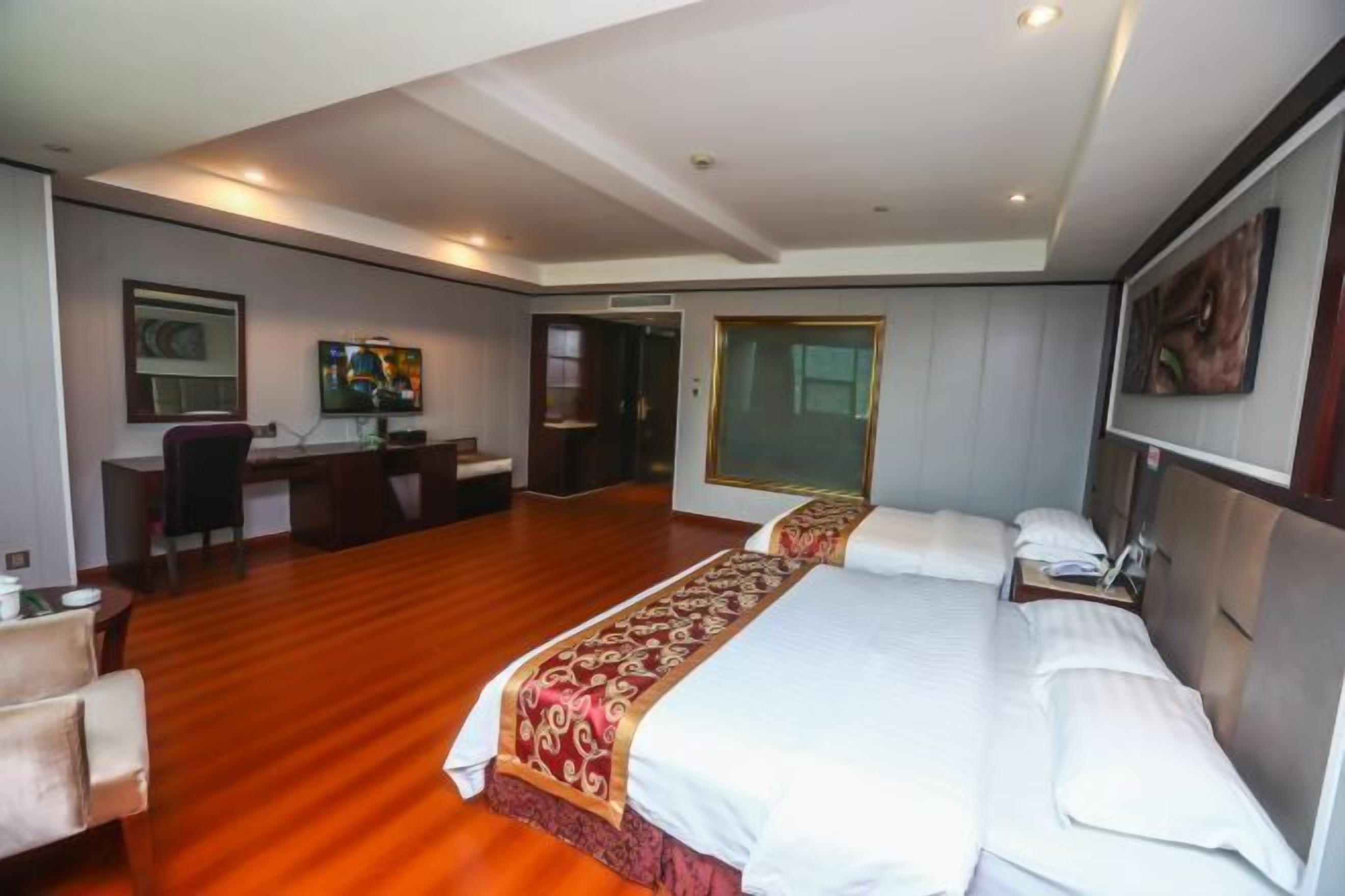 A hotel room with a large bed, a desk, a chair, and a television.