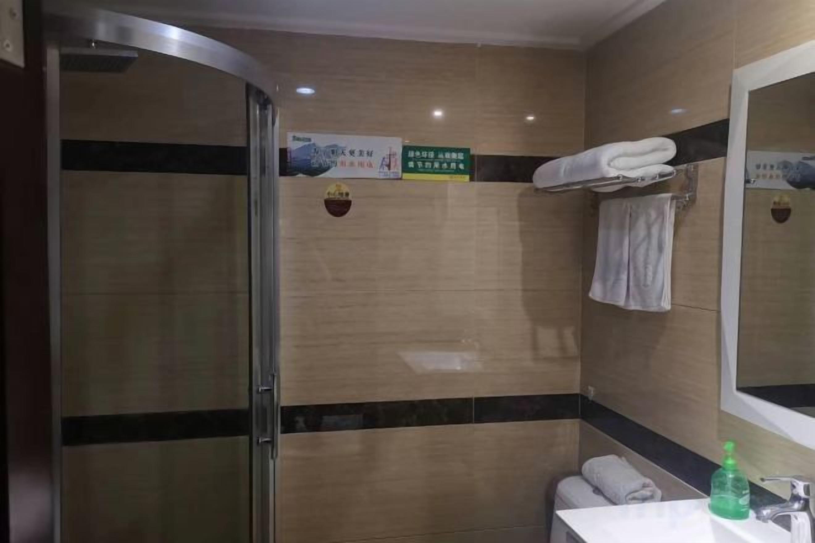 A bathroom with a shower, a sink, and a mirror. There are towels hanging on the wall and a sign above the mirror.