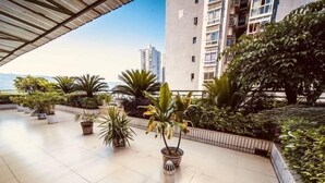 A rooftop terrace with potted plants, a metal railing, and a view of a tall building in the background. - Ru Jiang Hotel (Zhong County)