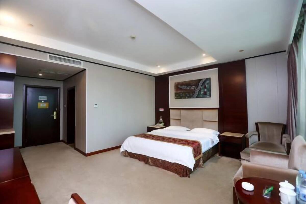 A hotel room with a bed, a chair, a desk, and a painting on the wall.