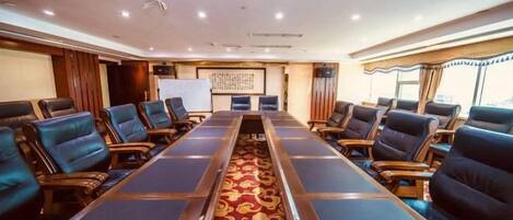 A conference room with a long table and multiple chairs, a whiteboard, and a decorative carpet.