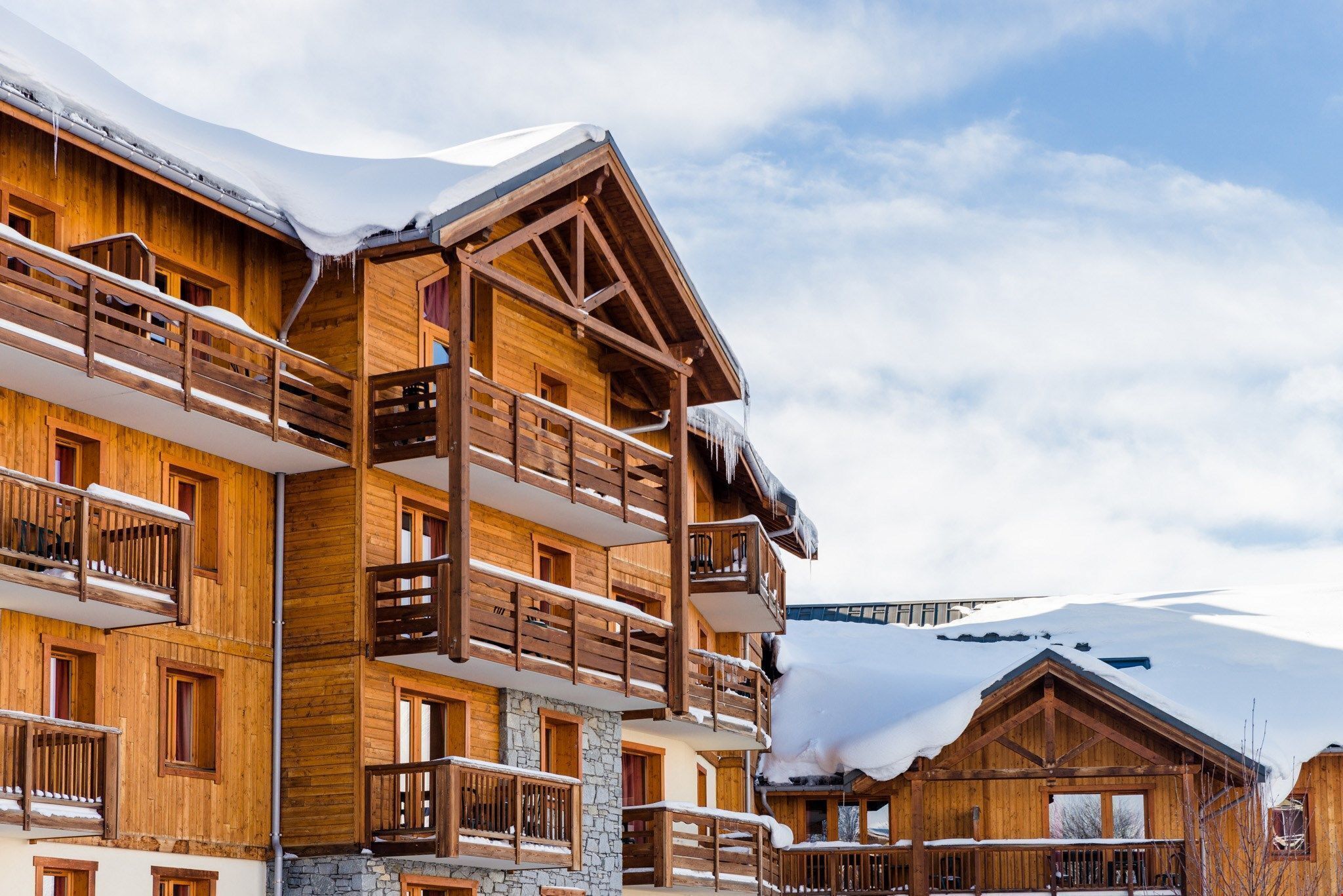 Un chalet en bois à plusieurs étages, doté de balcons, qui se dresse sur fond de montagnes enneigées.