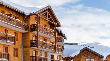 Un chalet en bois à plusieurs étages, doté de balcons, qui se dresse sur fond de montagnes enneigées.