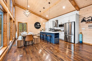 A modern kitchen with wooden floors, a central island, bar stools, and stainless steel appliances.