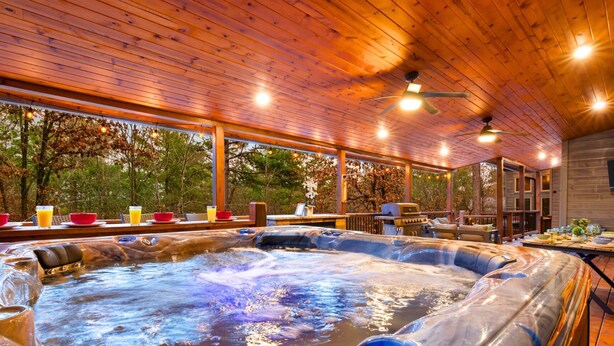Un bain à remous avec une terrasse en bois, un ventilateur de plafond et une vue sur les arbres.