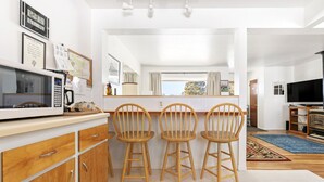 Una cocina moderna con armarios de madera, microondas y una barra con tres taburetes de madera.