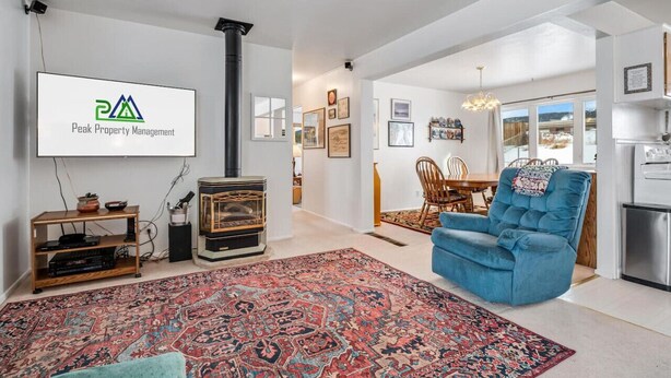 Una sala de estar con un televisor grande mostrando 'Peak Property Management', un sillón azul, un tapete estampado y un mueble bajo de madera.