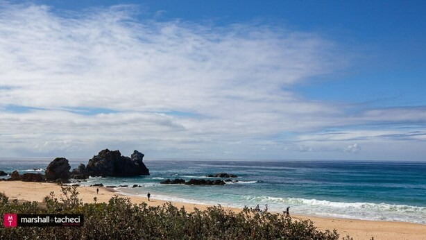 A beach with clear skies, rocky formations, and calm ocean waves.