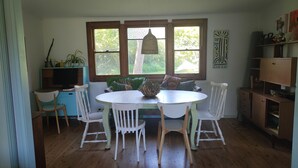 A dining area with a round table and four chairs, a bookshelf, and a window with a view of greenery.