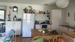 A compact kitchen with a refrigerator, stove, and various kitchen items. There is a dining table with chairs and a small seating area with a chair and cushions.
