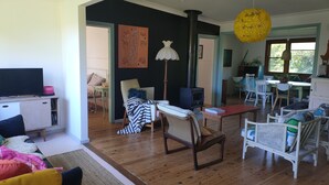 A spacious living room with a wooden floor, a black and white striped chair, a white armchair, and a dining area with a table and chairs.