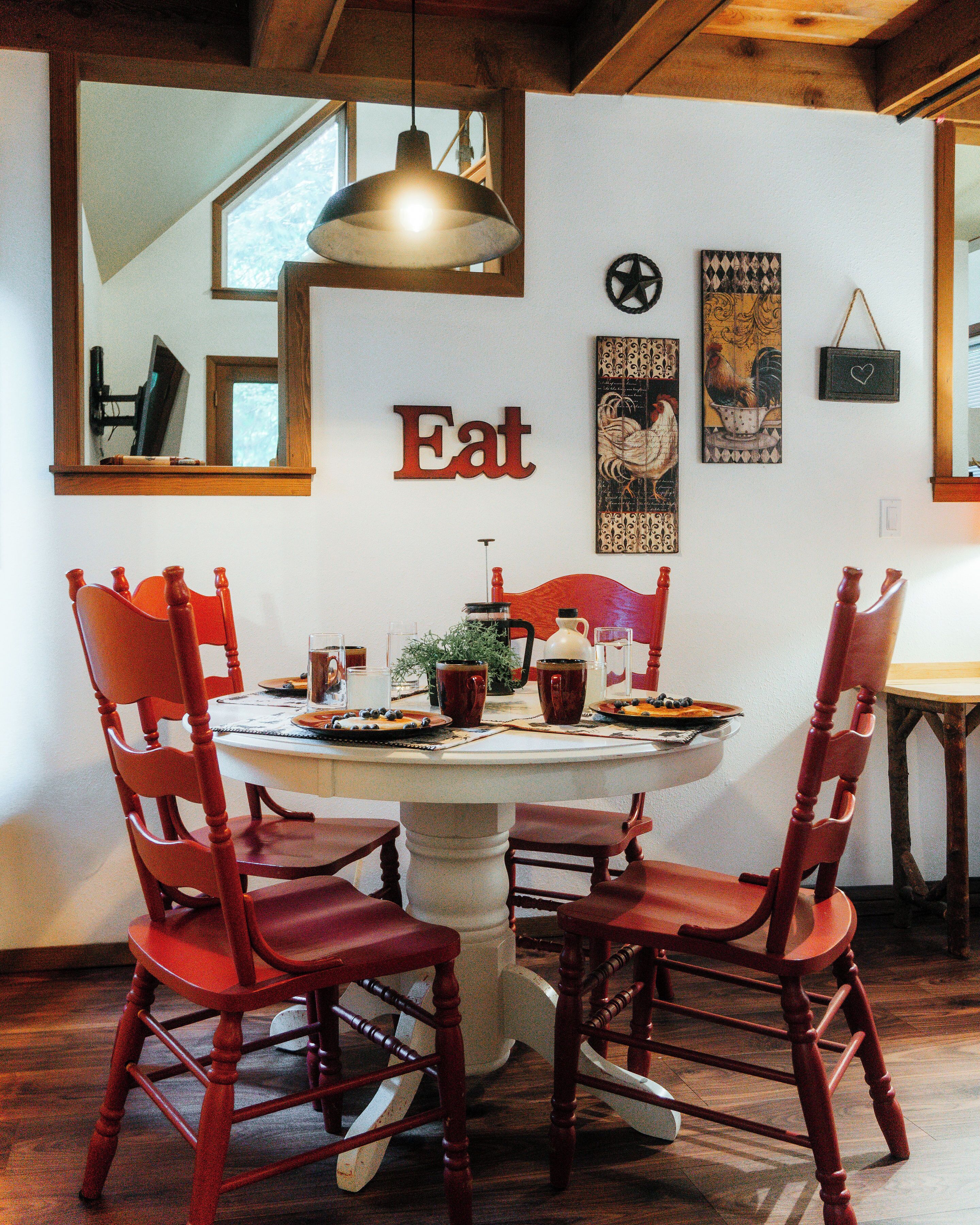 Een eetgedeelte met een ronde tafel, rode stoelen en een bord met de tekst 'Eat' aan de muur.