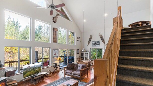 Un vaste espace de vie doté d’une cheminée, de grandes fenêtres, d’un escalier en bois et d’un coin salon confortable.