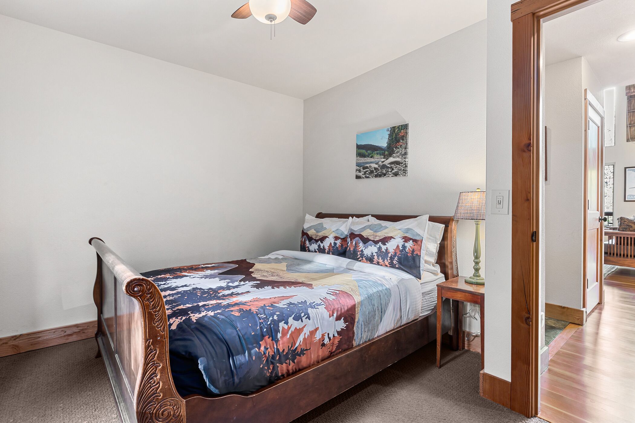 A bedroom with a wooden bed, a nightstand, a lamp, and a painting on the wall.