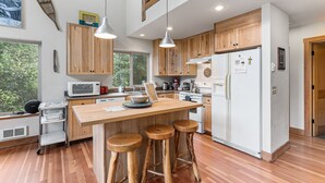 Une cuisine moderne avec des meubles en bois, un îlot central doté de tabourets, un four à micro-ondes et un réfrigérateur.