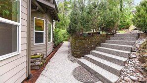 A house with a stone staircase leading to a wooden deck, surrounded by trees and a stone wall. - Valley View- best view, private acreage, ping pong (Gold Bar)