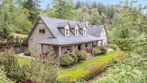 A two-story house with a wrap-around porch, surrounded by lush greenery and a well-maintained garden. - Valley View- best view, private acreage, ping pong (Gold Bar)
