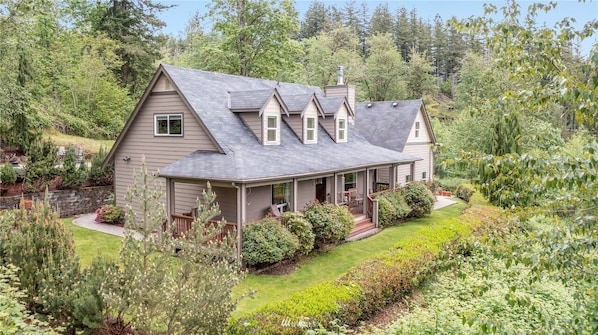 A two-story house with a wrap-around porch, surrounded by lush greenery and a well-maintained garden.