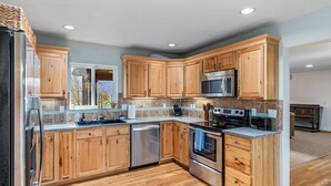 A modern kitchen with wooden cabinets, stainless steel appliances, and a tiled backsplash. - Valley View- best view, private acreage, ping pong (Gold Bar)