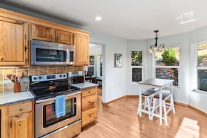 A kitchen with wooden cabinets, stainless steel appliances, a granite countertop, and a dining area with white chairs.