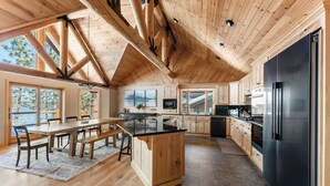 A modern kitchen with wooden beams, a large island, and a black refrigerator. - Lakeside Serenity. Mountain Views. Spa. BBQ. Games (Big Bear Lake)