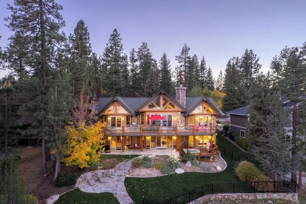 A multi-story log cabin with a deck, surrounded by a forest.