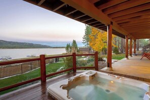 A wooden deck with a hot tub, a view of a lake, and a fenced area.
