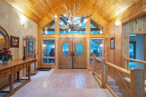 A wooden interior with a large chandelier, double doors with glass panels, and a wooden staircase.