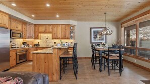 Una cocina con armarios de madera, una isla central y una zona de comedor con sillas y una mesa.