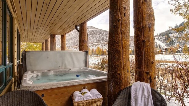 Una terraza de madera con un jacuzzi, sillas de mimbre y un cesto de toallas.