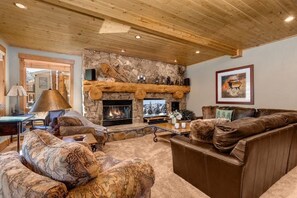 A cozy living room with a stone fireplace, wooden ceiling, and a large sofa.