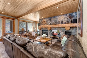 A cozy living room with leather sofas, a stone fireplace, and wooden beams on the ceiling.