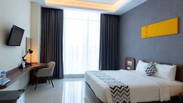 A hotel room with a bed, a desk with a chair, a television, and a large window with curtains.