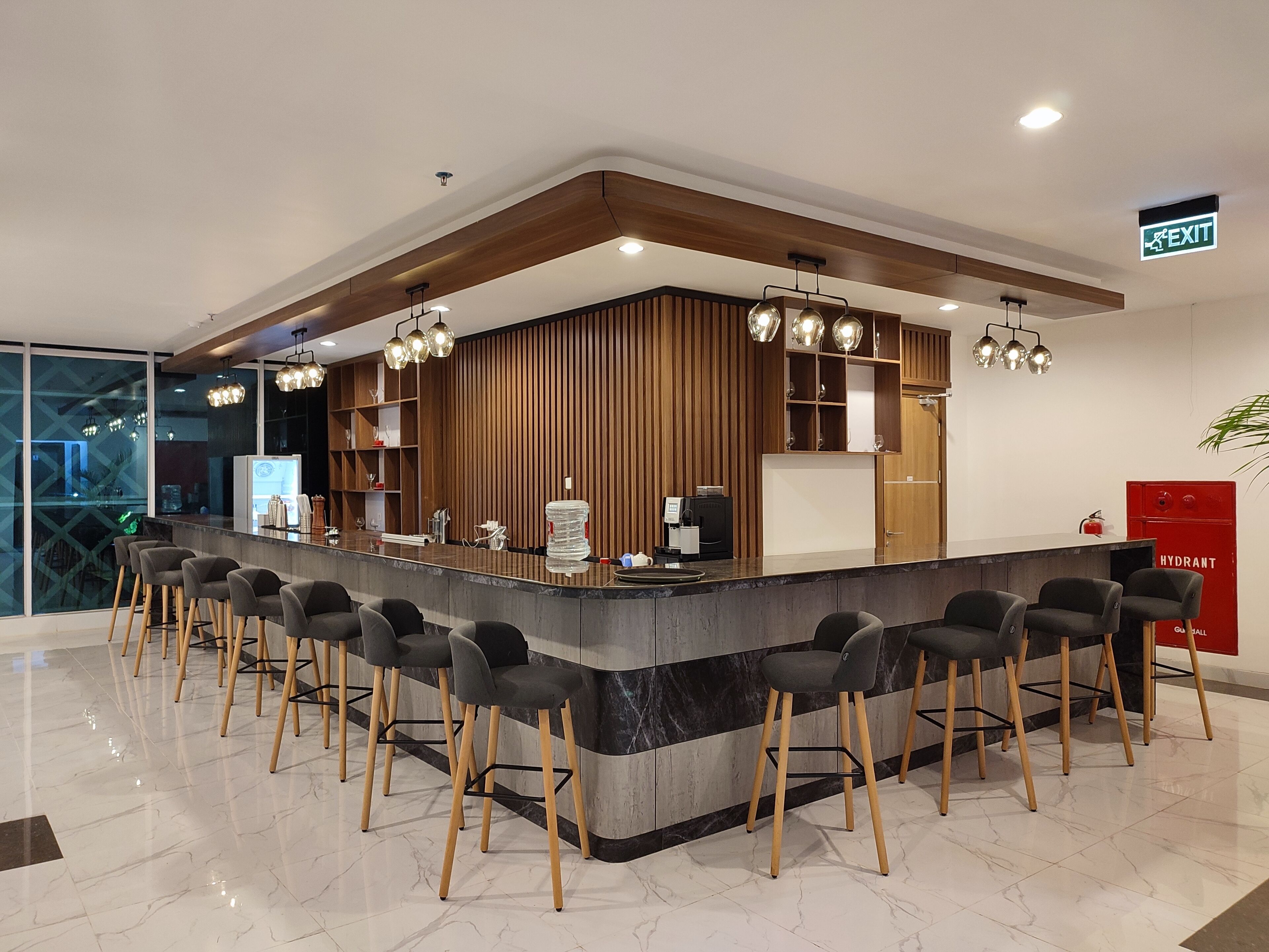Uma área de bar moderna com bancada de mármore, detalhes em madeira e vários banquetes.