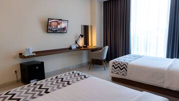 A hotel room with two beds, a desk with a chair, a small refrigerator, a lamp, and a picture on the wall.