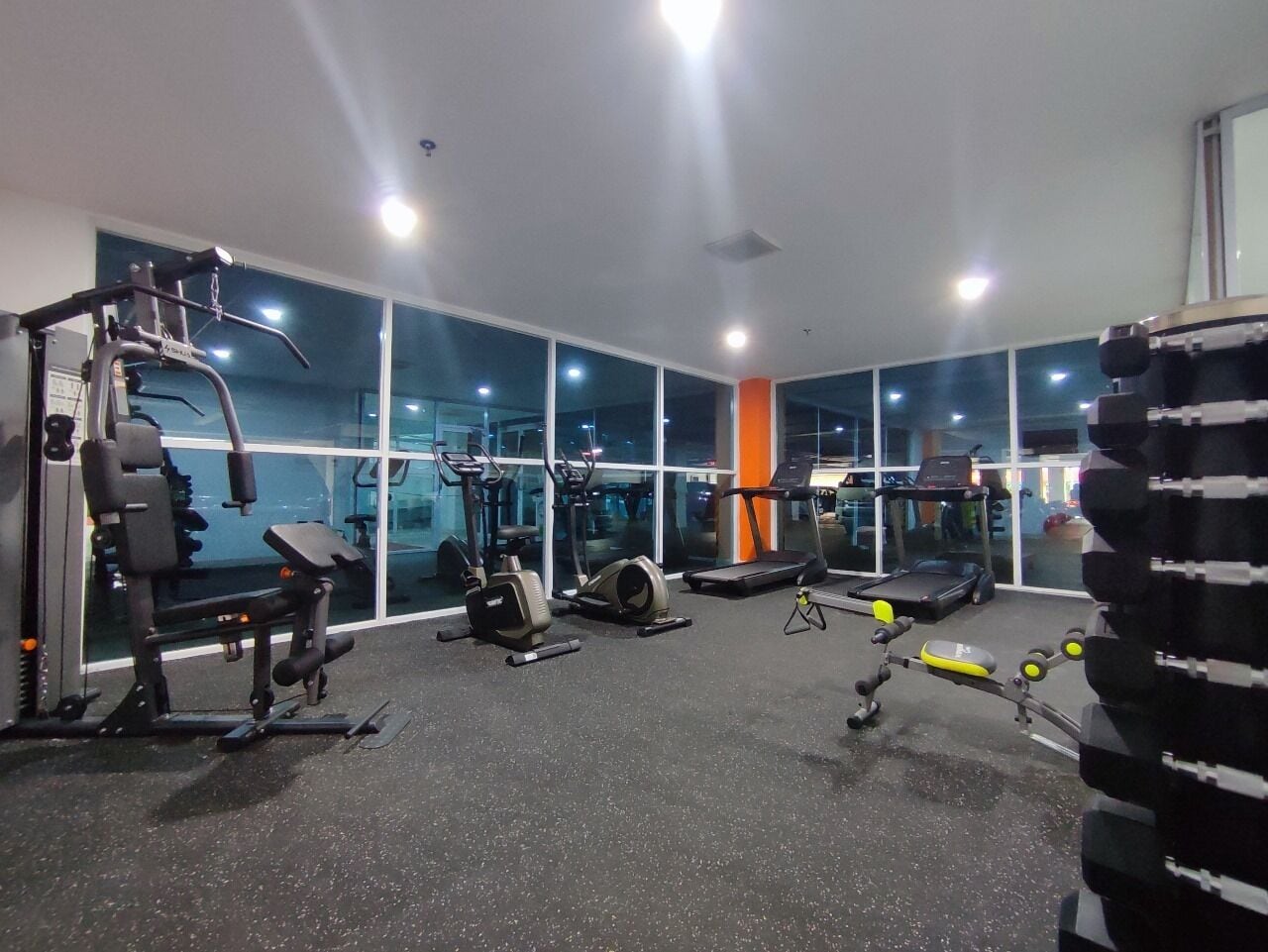 Un gimnasio con diverso equipo de ejercicio, ventanas amplias y una cinta de correr.