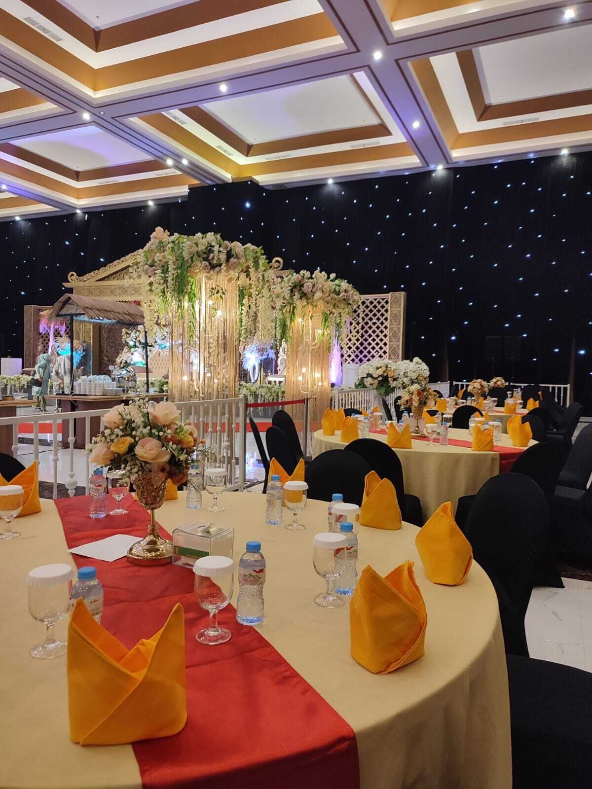 Un salón de banquetes con mesas redondas, servilletas amarillas y centros de mesa florales.