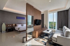 A modern hotel room with a bed, sofa, TV, and a view of the outdoors. - UNHAS HOTEL & CONVENTION (Makassar)