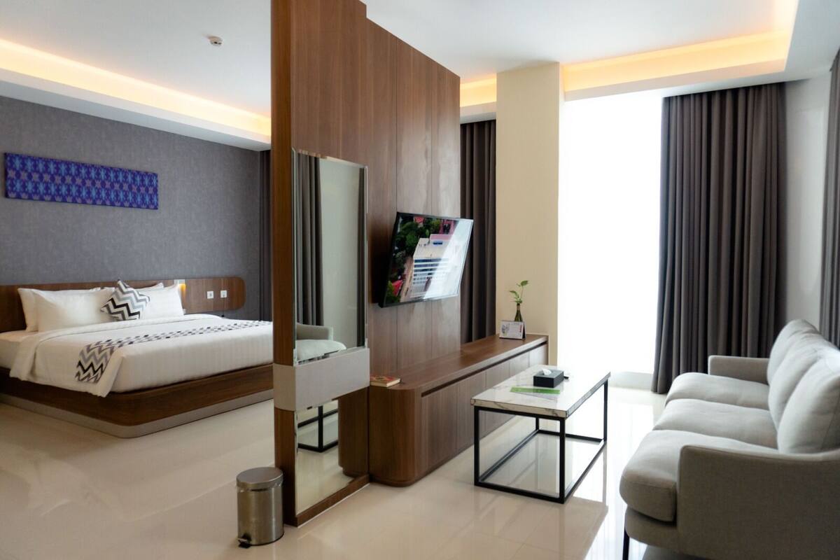 A modern hotel room with a bed, a TV, a sofa, and a desk.