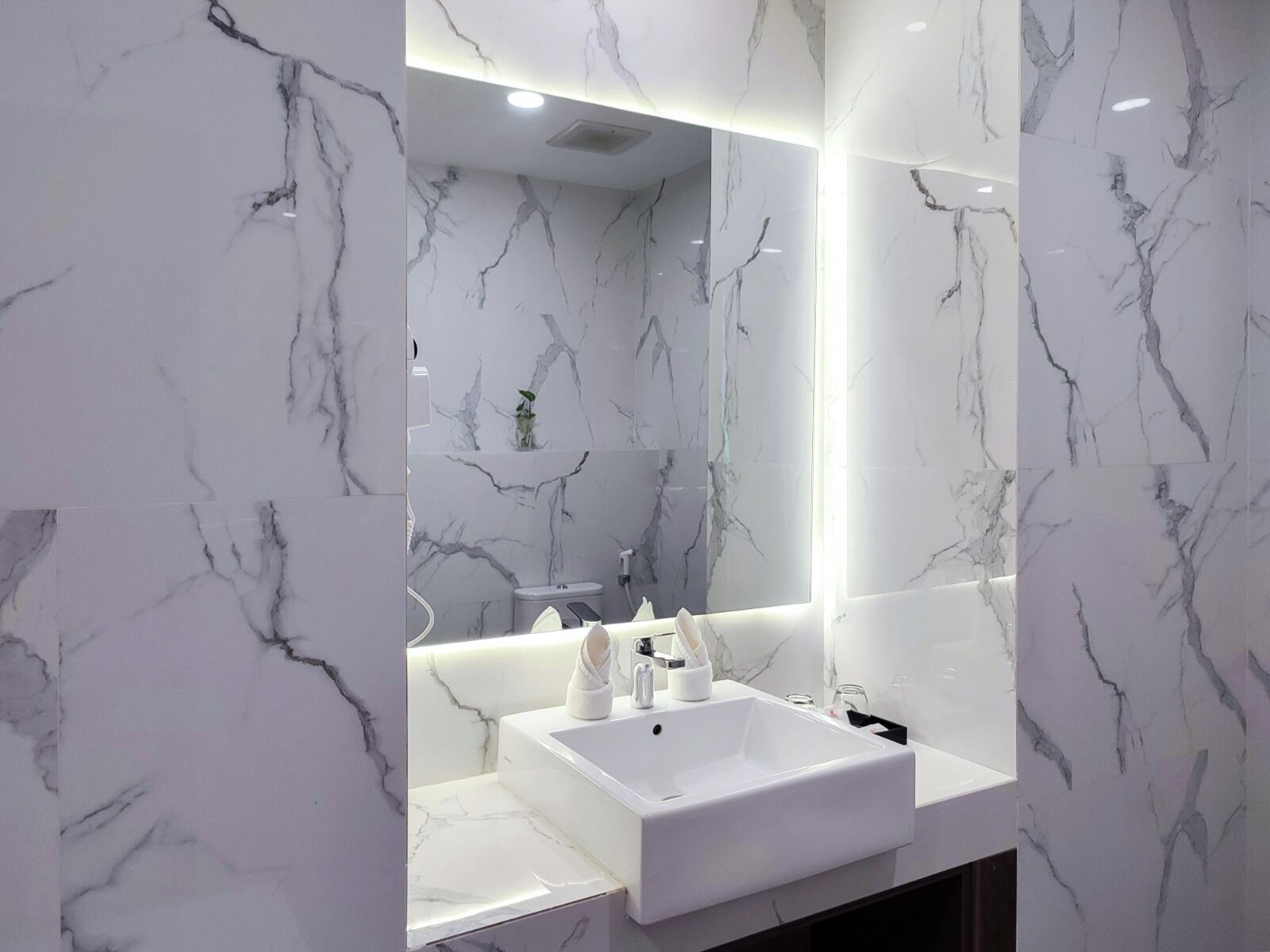 A modern bathroom with marble walls and a large mirror.