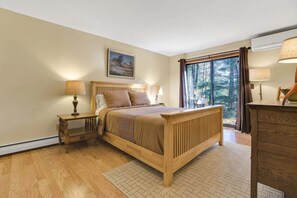 A bedroom with a wooden bed, a nightstand, a dresser, a window with curtains, and a painting on the wall.