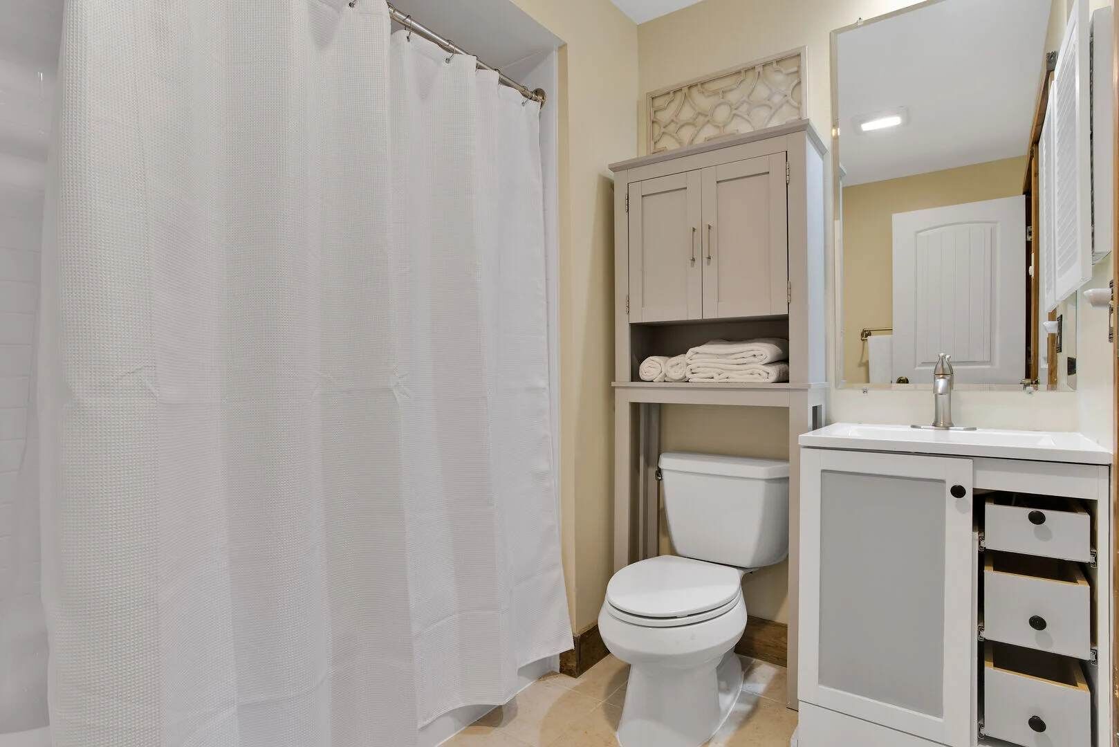 Ein Badezimmer mit Toilette, Duschvorhang, Waschbecken und einem Schrank.