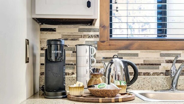 Cuina amb una cafetera Keurig, una tetera, un molinet de cafè i una forna per a cafè al taulell.
