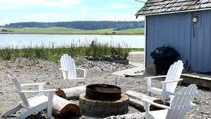 A lakeside cabin with a fire pit and white Adirondack chairs. - West Beach Bungalow: Whidbey Waterfront Beach House VIEWS + 5 Star Reviews (Oak Harbor)