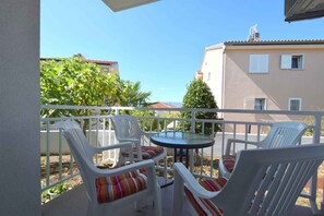 A balcony with white plastic chairs and a small round table, overlooking a residential area with buildings and greenery.